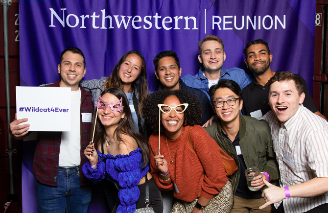 Nine people in front a Northwestern Reunion backdrop, one holding a #Wildcats4Ever sign
